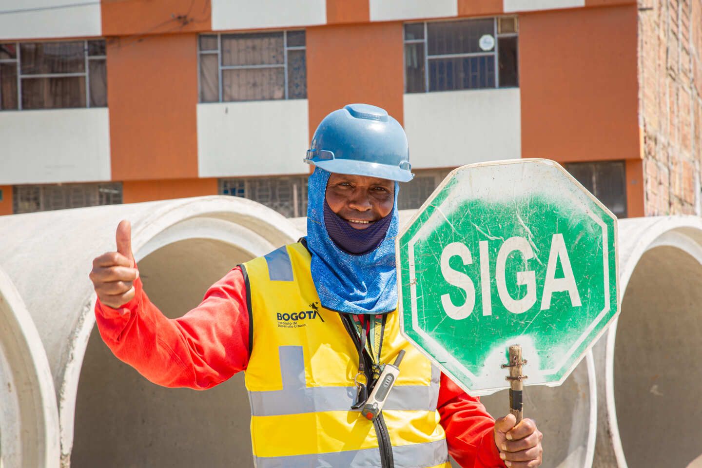 Empleado de obra sostiene en una mano un letrero que dice siga y en la otra mano tiene el pulgar arriba