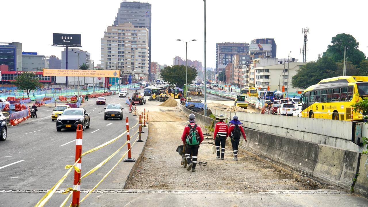 Tres trabajadores caminan sobre la obra de la avenida 68. Uno de ellos transporta una carretilla